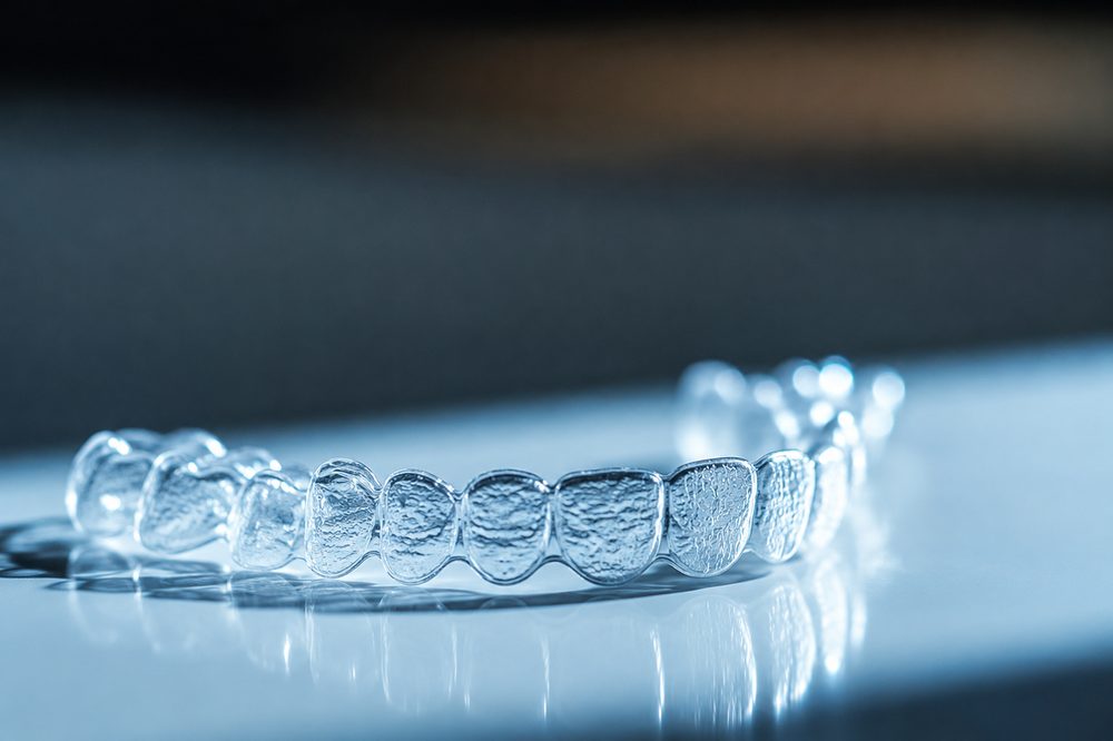 transparent orthodontic aligners sitting on a clean clinical surface with soft blue highlights